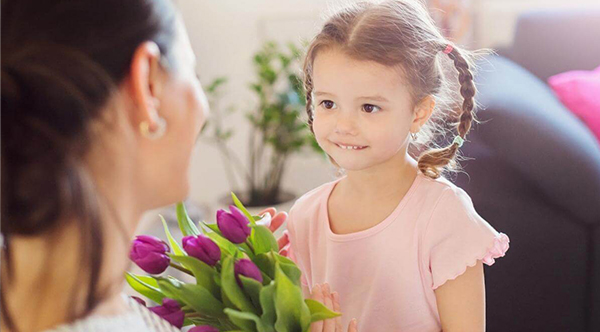 Malá holčička gratuluje mámě ke Dni matek s kyticí fialových tulipánů